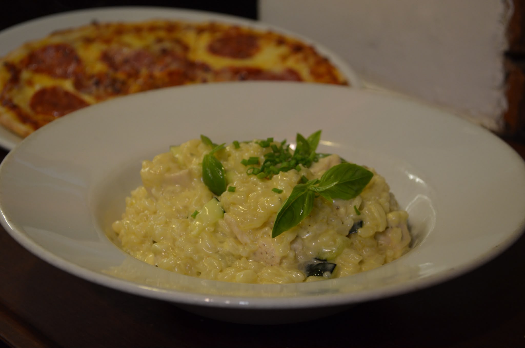 Creamy chicken and courgette risotto garnished with basil, with a pepperoni pizza behind