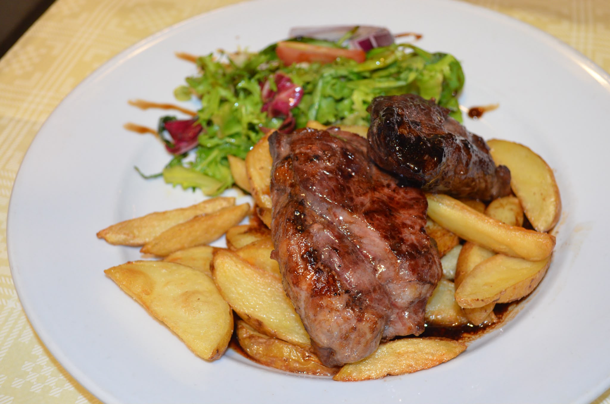 Close-up of a juicy chargrilled steak resting on golden potato wedges with salad