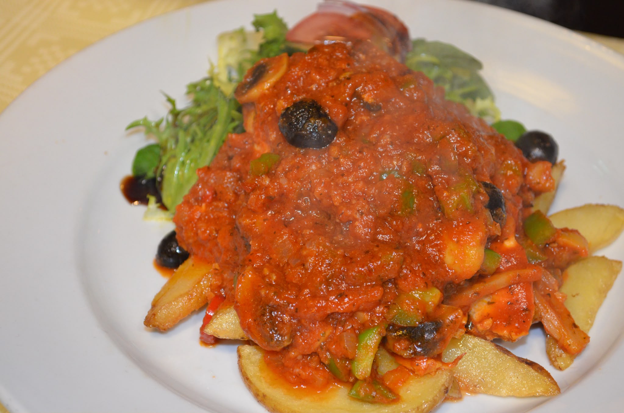 Chicken in a rich tomato sauce with olives and peppers, served over sautéed potatoes