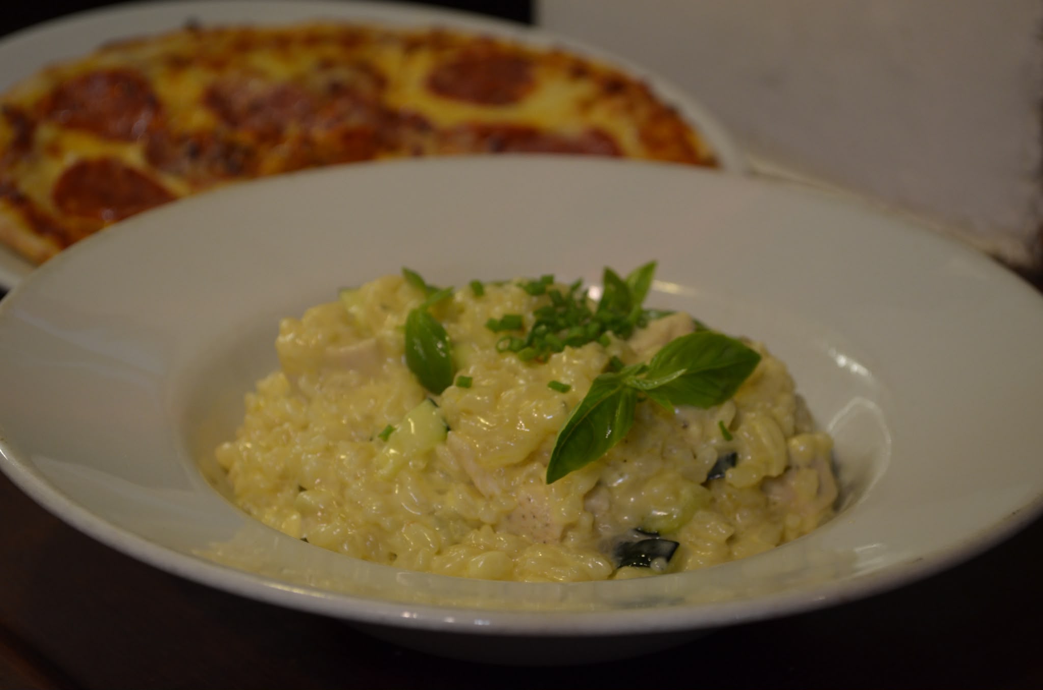 Bowl of creamy risotto topped with chives and fresh basil leaves