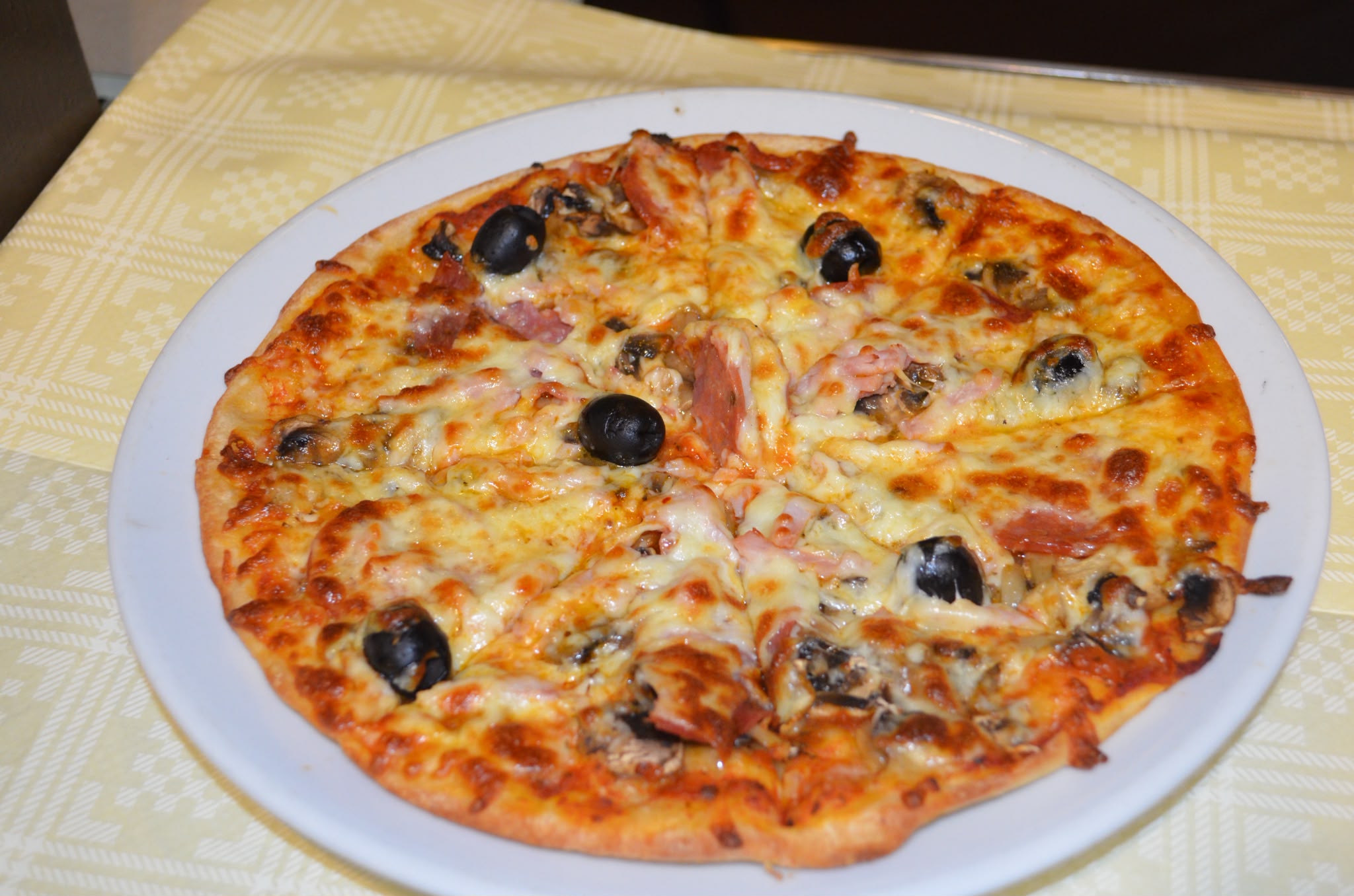 Stone-baked pizza topped with ham, mushrooms and black olives